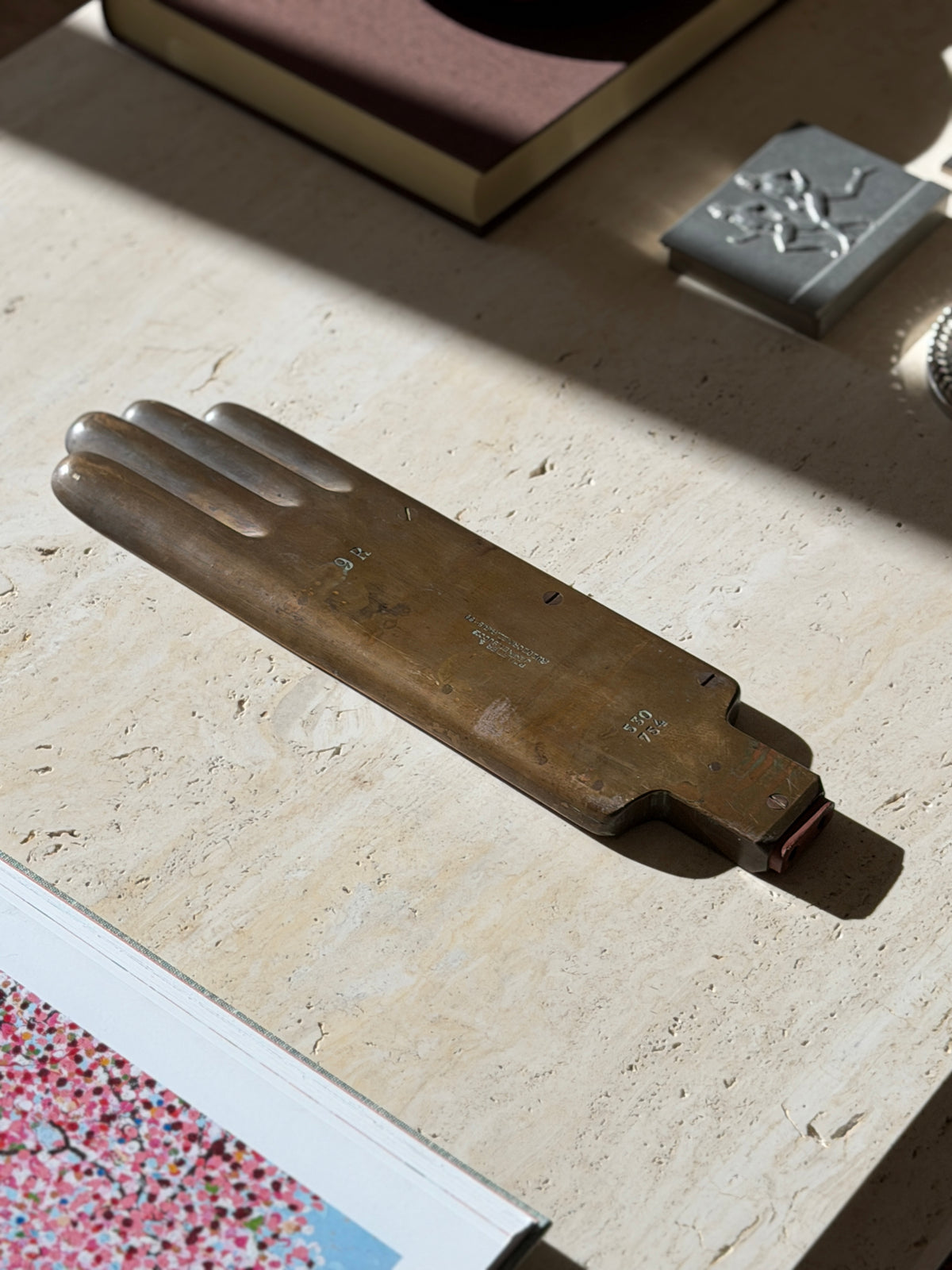 French brass glove form on a travertine coffee table beside an open art book, a brown book and a pewter box with runners in relief