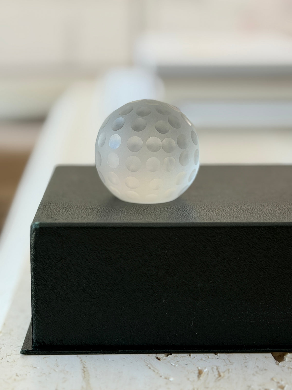 Eye-level front view of Cartier frosted glass golf ball desk accessory on black pedestal display box