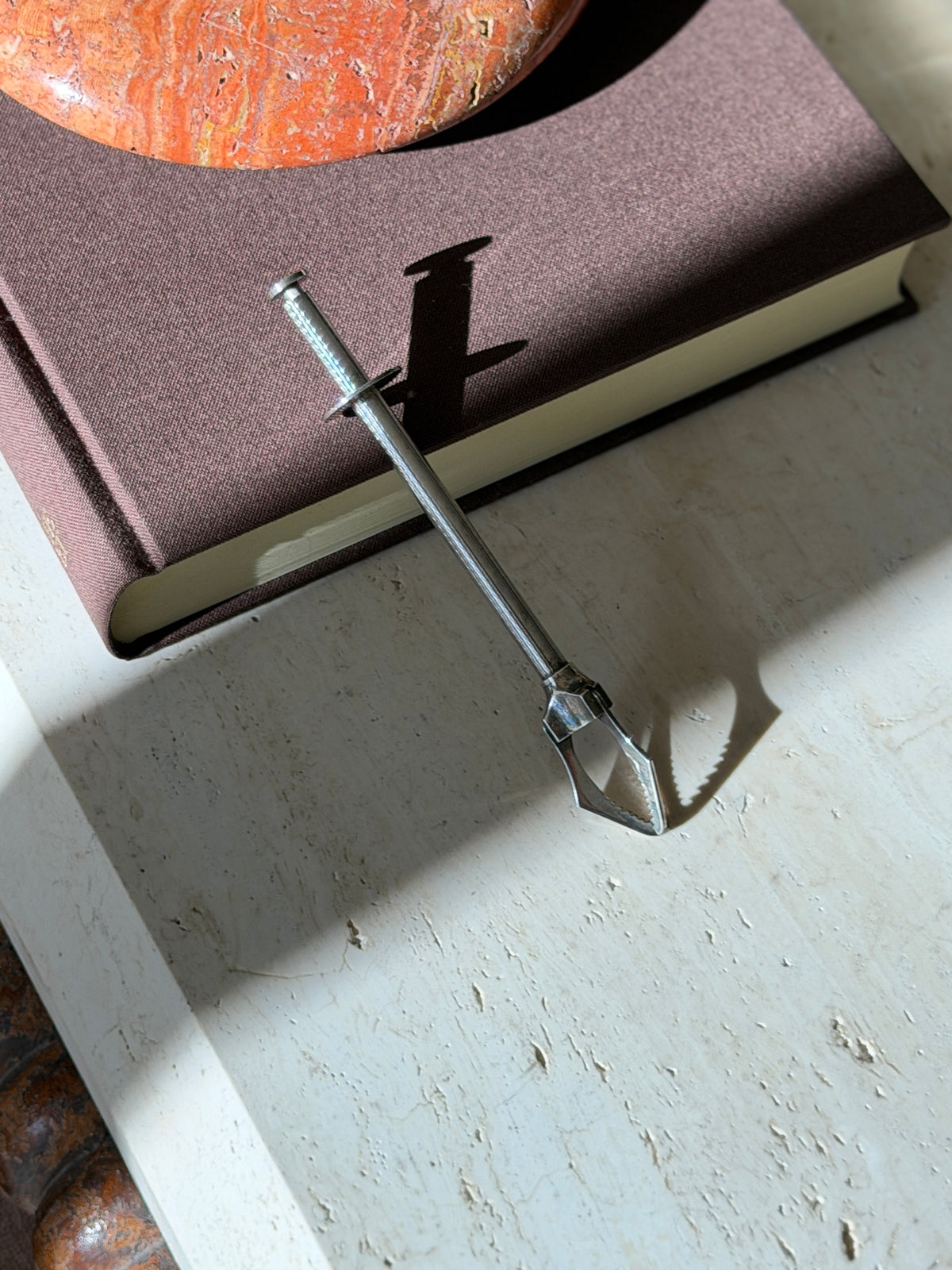 Christofle mechanical tongs with an engine turned silver plate handle resting on a brown book beside a red stone ashtray, serrated claw jaws on travertine