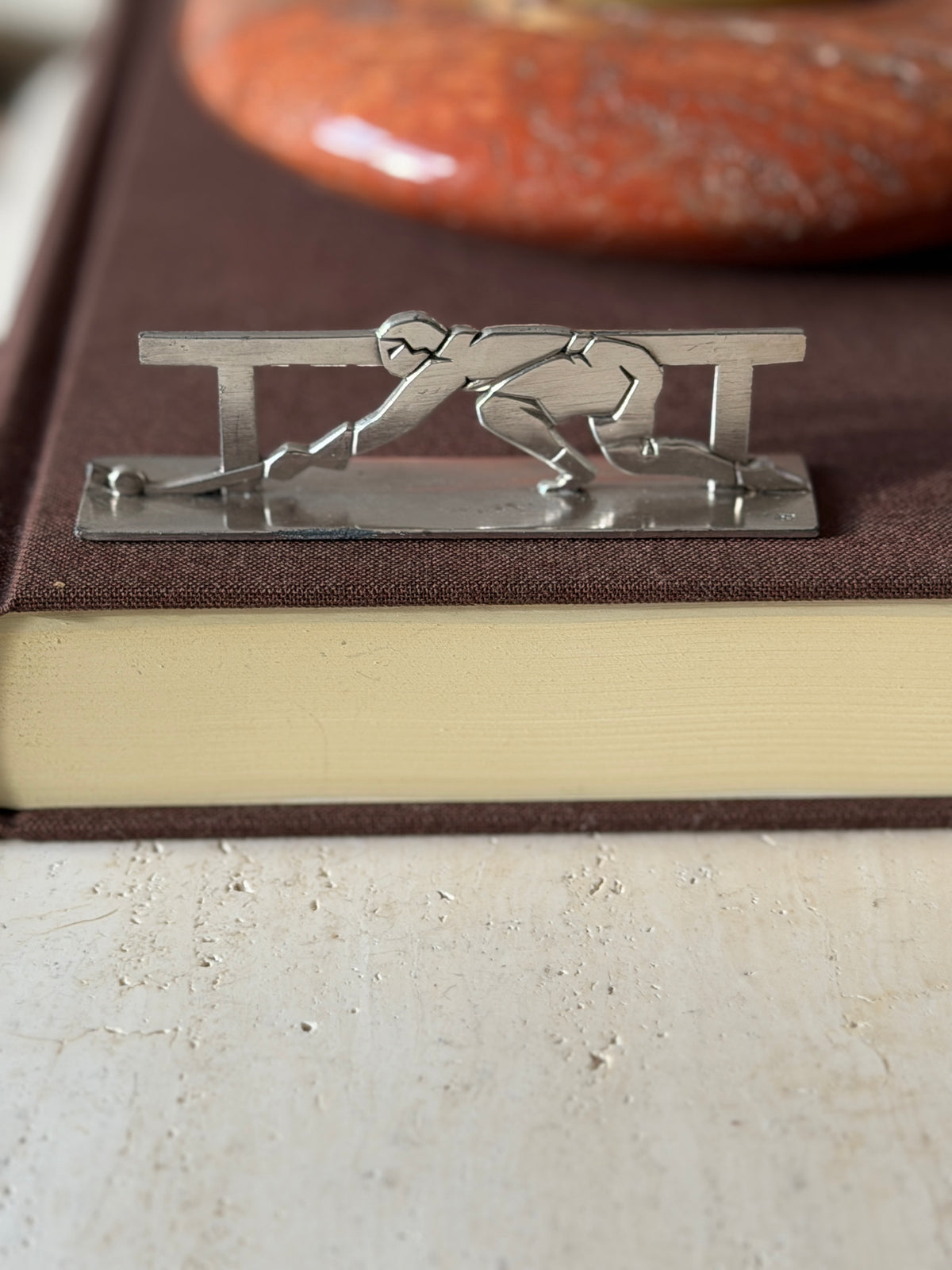 Fencer knife rest on a brown book, a masked fencer in a deep lunge with foil extended between two rail posts
