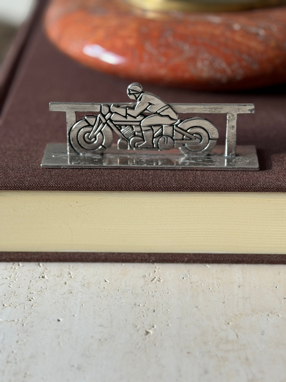Motorcycle knife rest on a brown book, a helmeted rider crouched over a geometric Art Deco motorbike