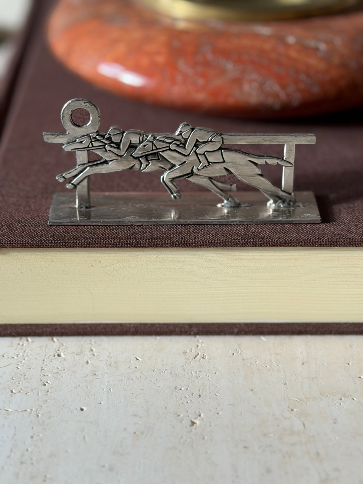 Horse racing knife rest on a brown book, two jockeys neck and neck at the rail with a ring finial at one end