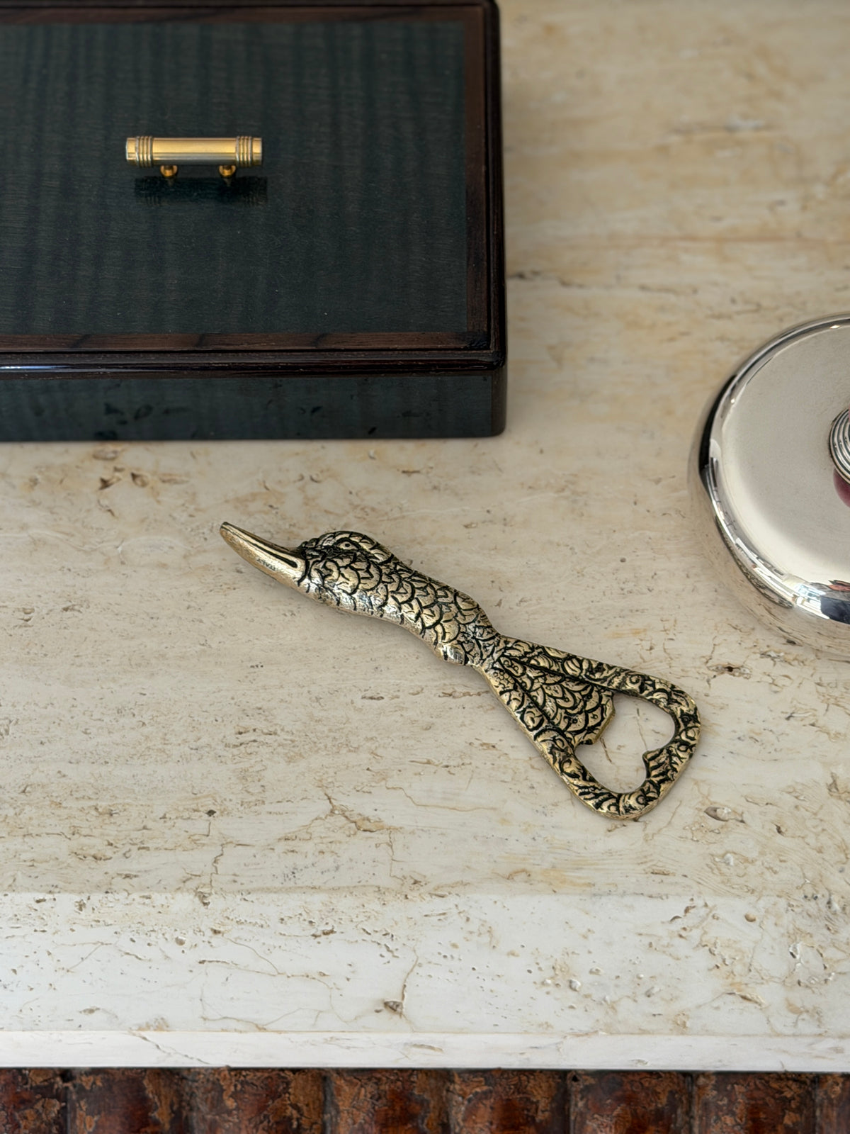 Overhead view of the duck head opener with chased feathers and a heart shaped opening, below a dark box with a brass handle
