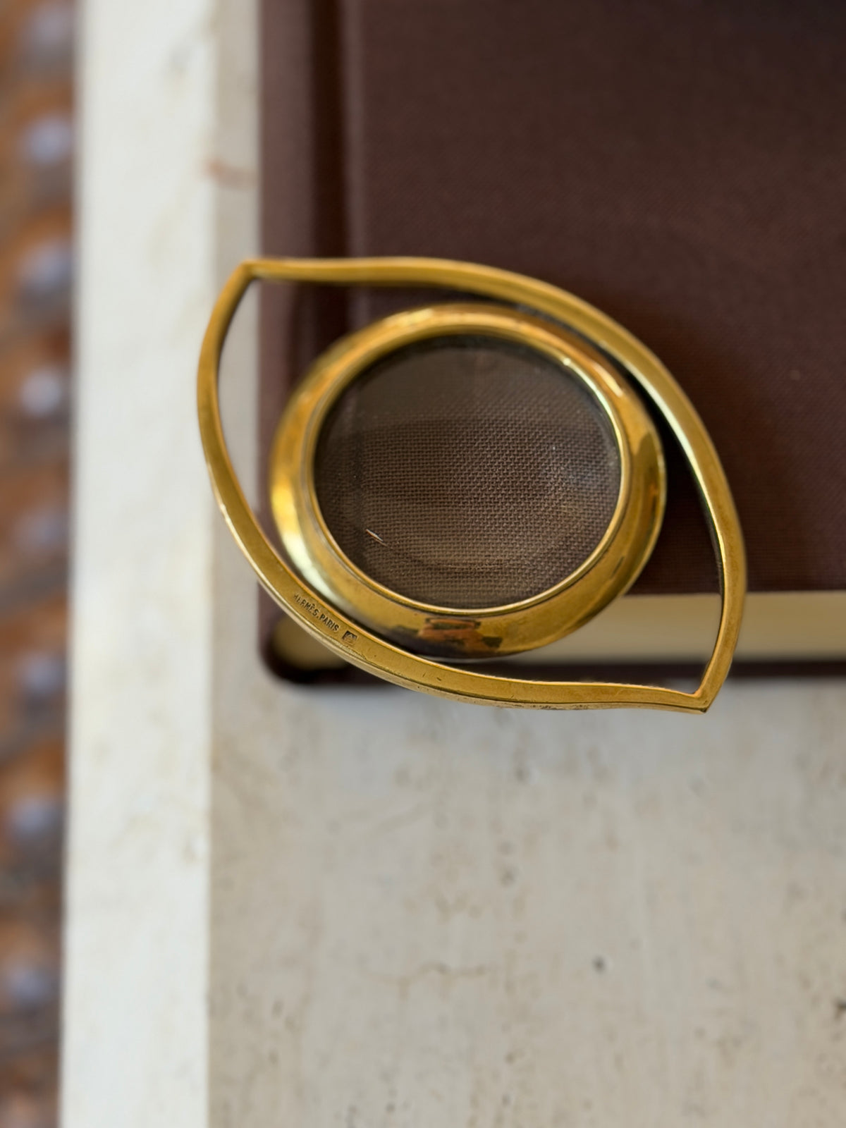 Close detail of the gilt eye frame showing the stamped Hermes Paris mark beside the round magnifying lens
