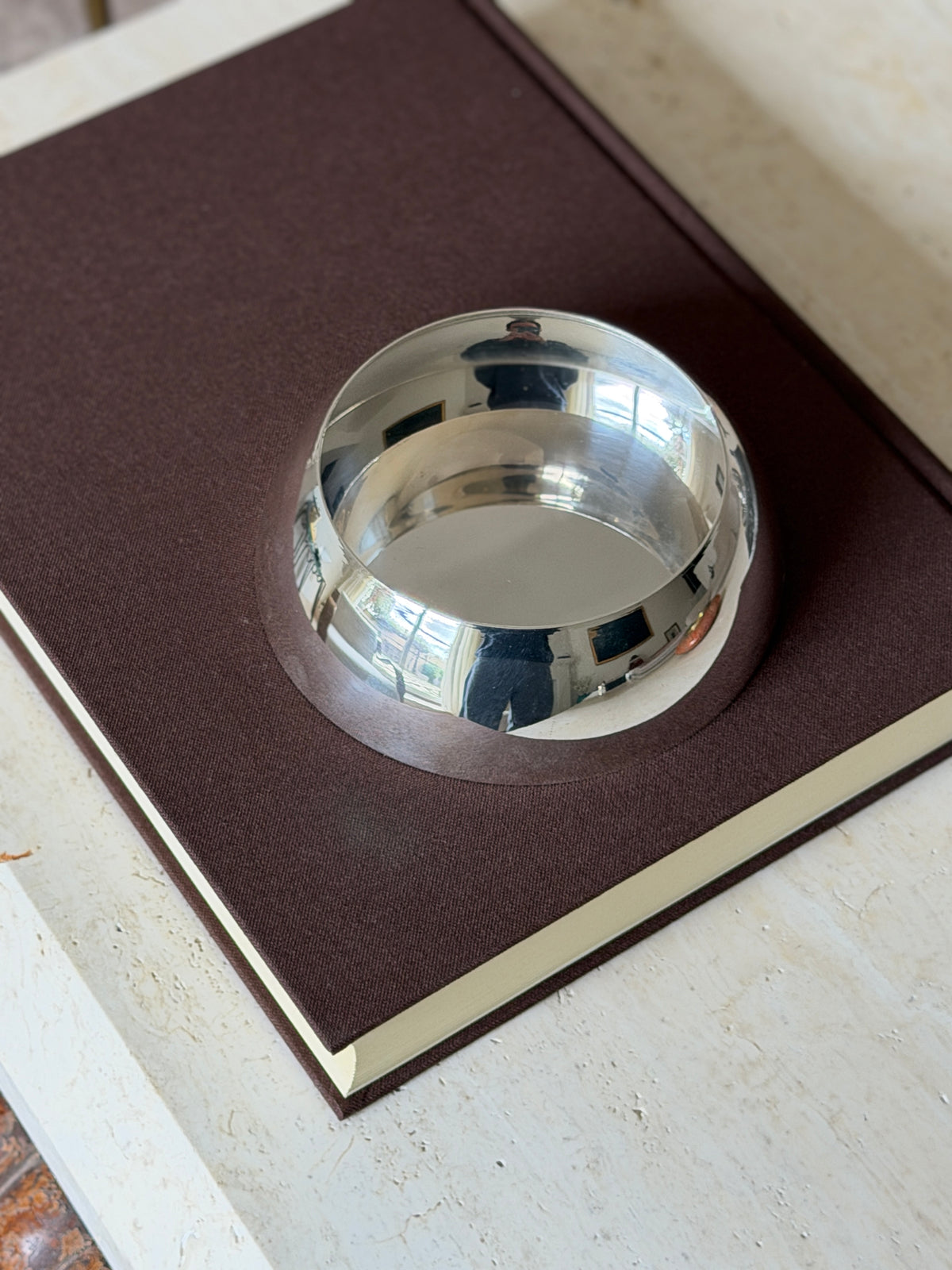 Empty Hermes bottle coaster on a brown clothbound book, the rounded silver wall and plain polished base in view