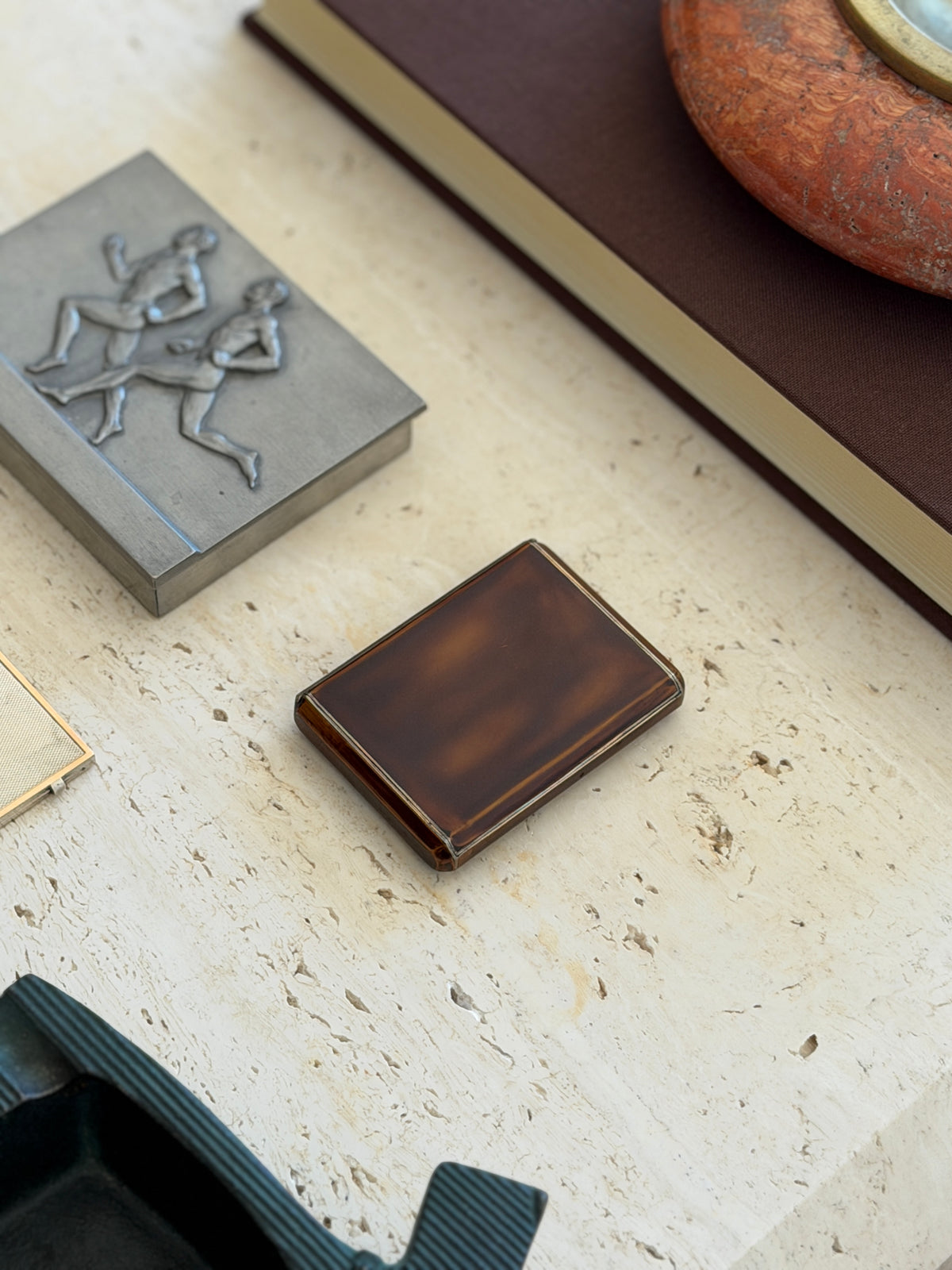 Overhead view of the Keller brown lacquer box on travertine between a pewter runners box and a brown book with red stone ashtray