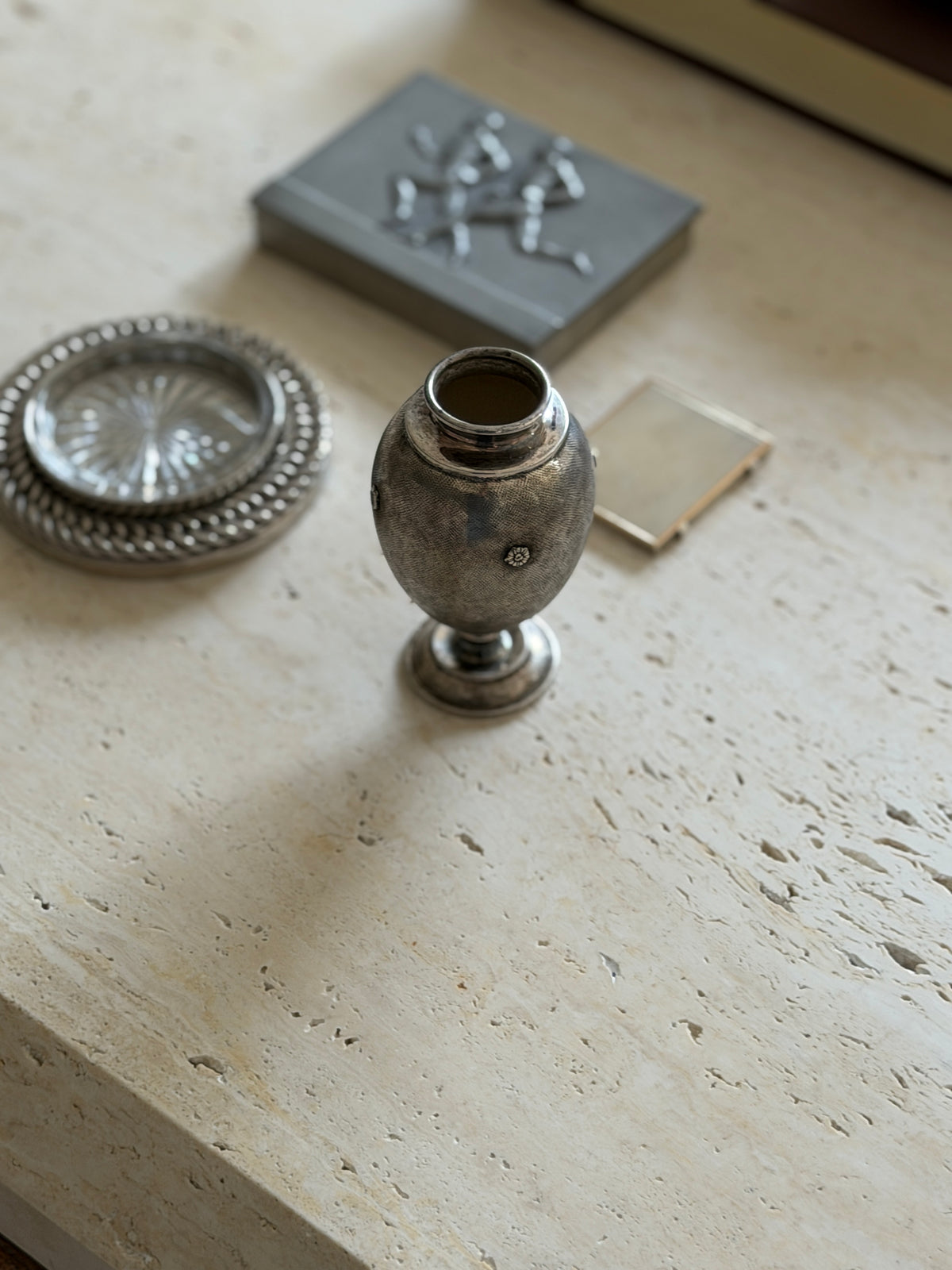 Mario Buccellati silver vase on travertine, an egg shaped body with fine textured engraving and applied floral rosettes, a chain link coaster and pewter box nearby