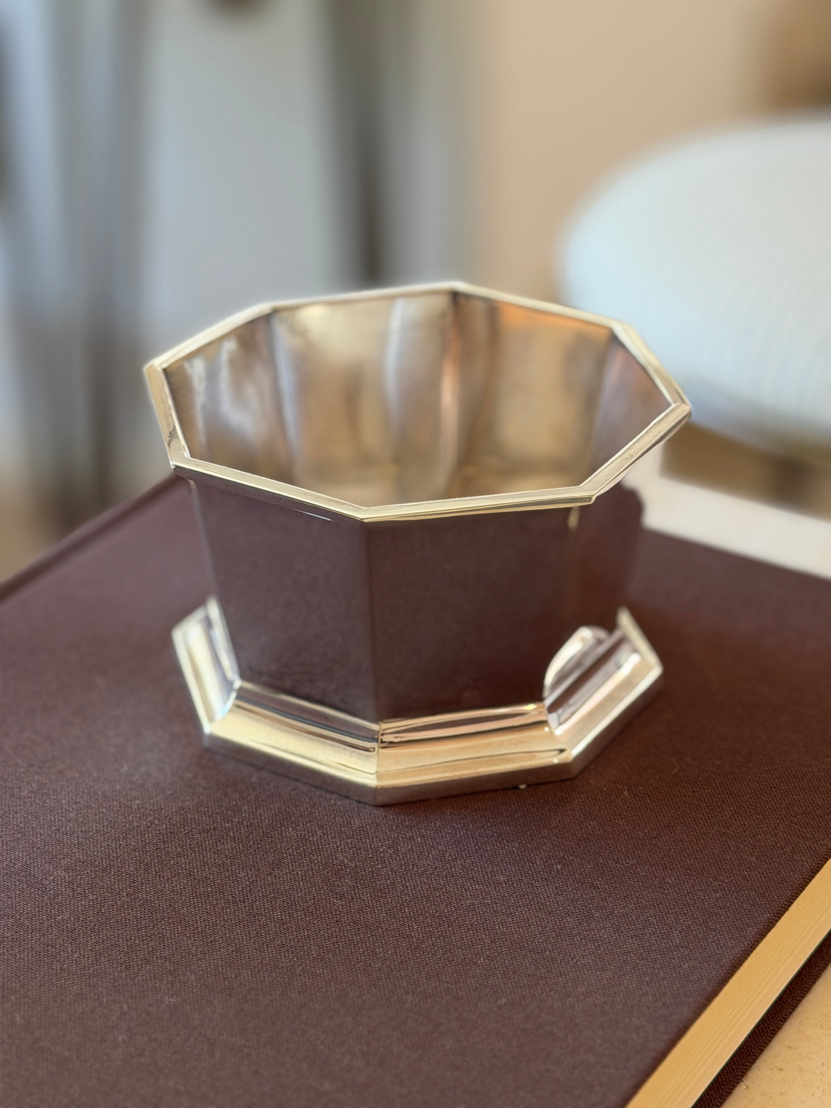 Angled view of the Kingsburgh nut bowl on a brown book, the mirror finish panels reflecting a soft lit room
