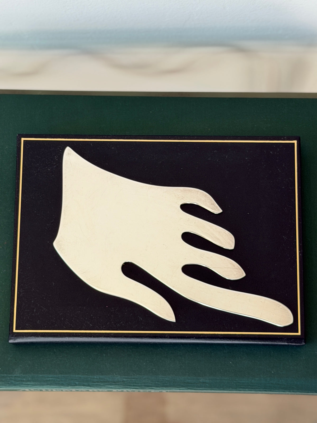Overhead view of the minimalist silver hand centered on a black book cover with a gold border, the fingers sweeping to the right