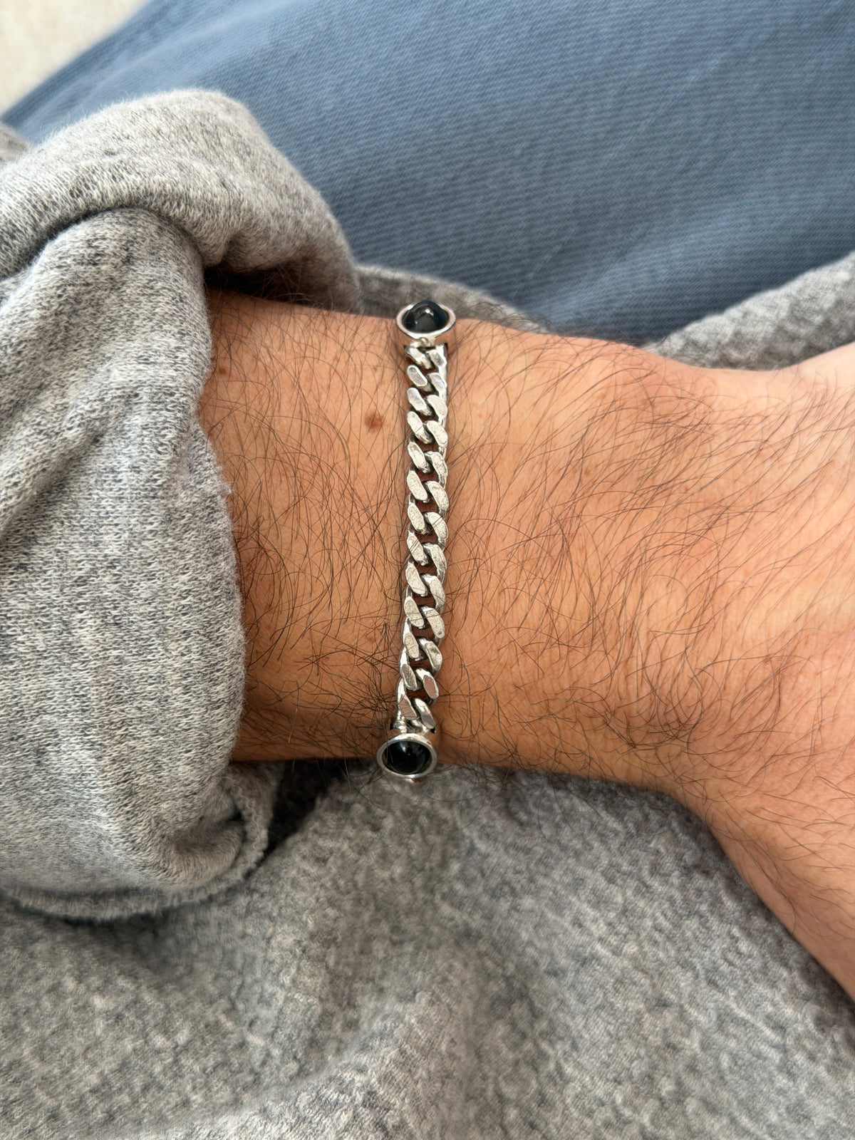 Sterling curb bracelet with three onyx cabochons draped from a brown book onto travertine in raking sunlight, ending in a spring ring clasp