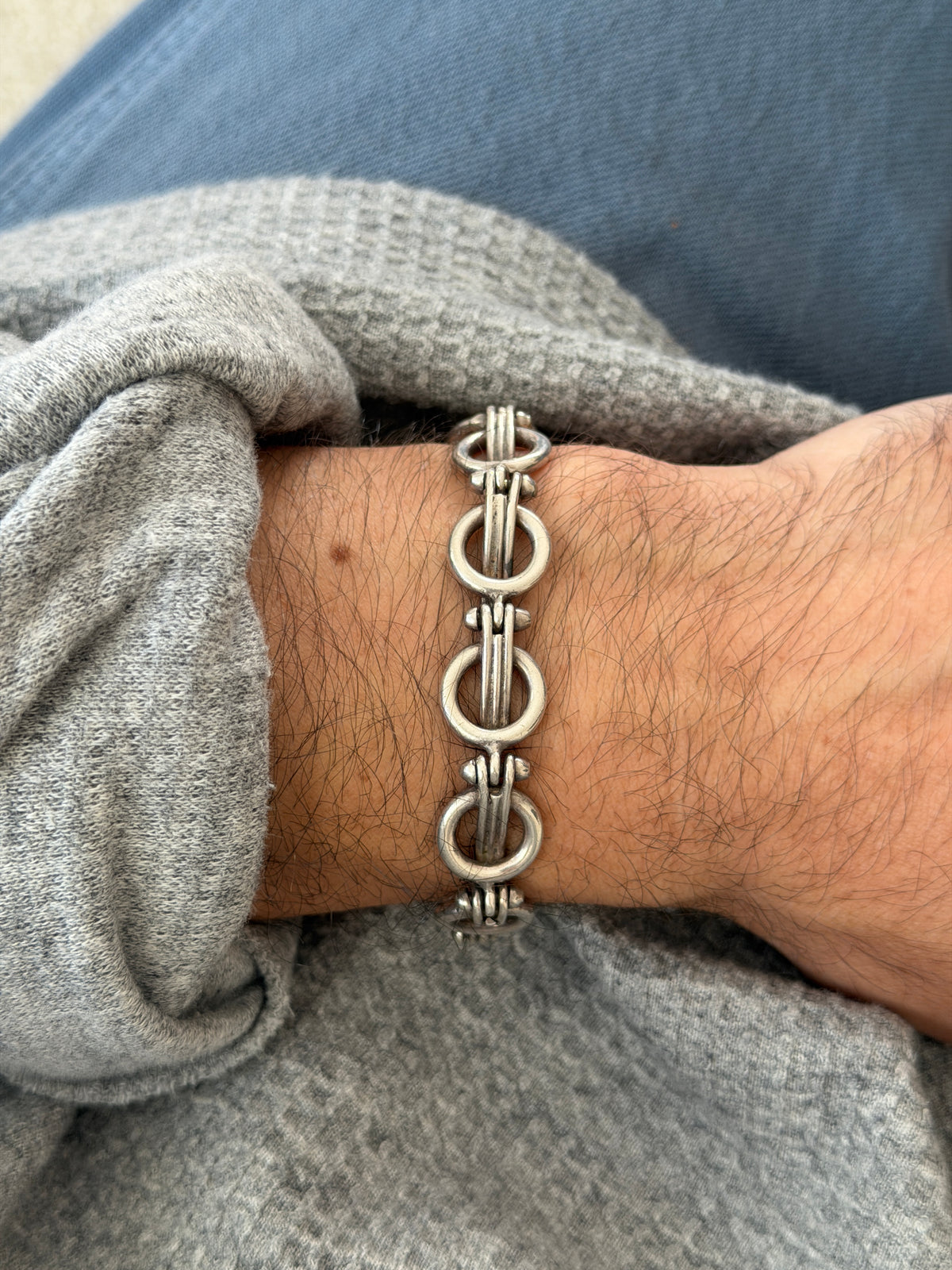 Vintage Mexican sterling silver bracelet of round rings joined by bundled parallel bars with studded ends, worn on the wrist over a gray sweater and blue denim