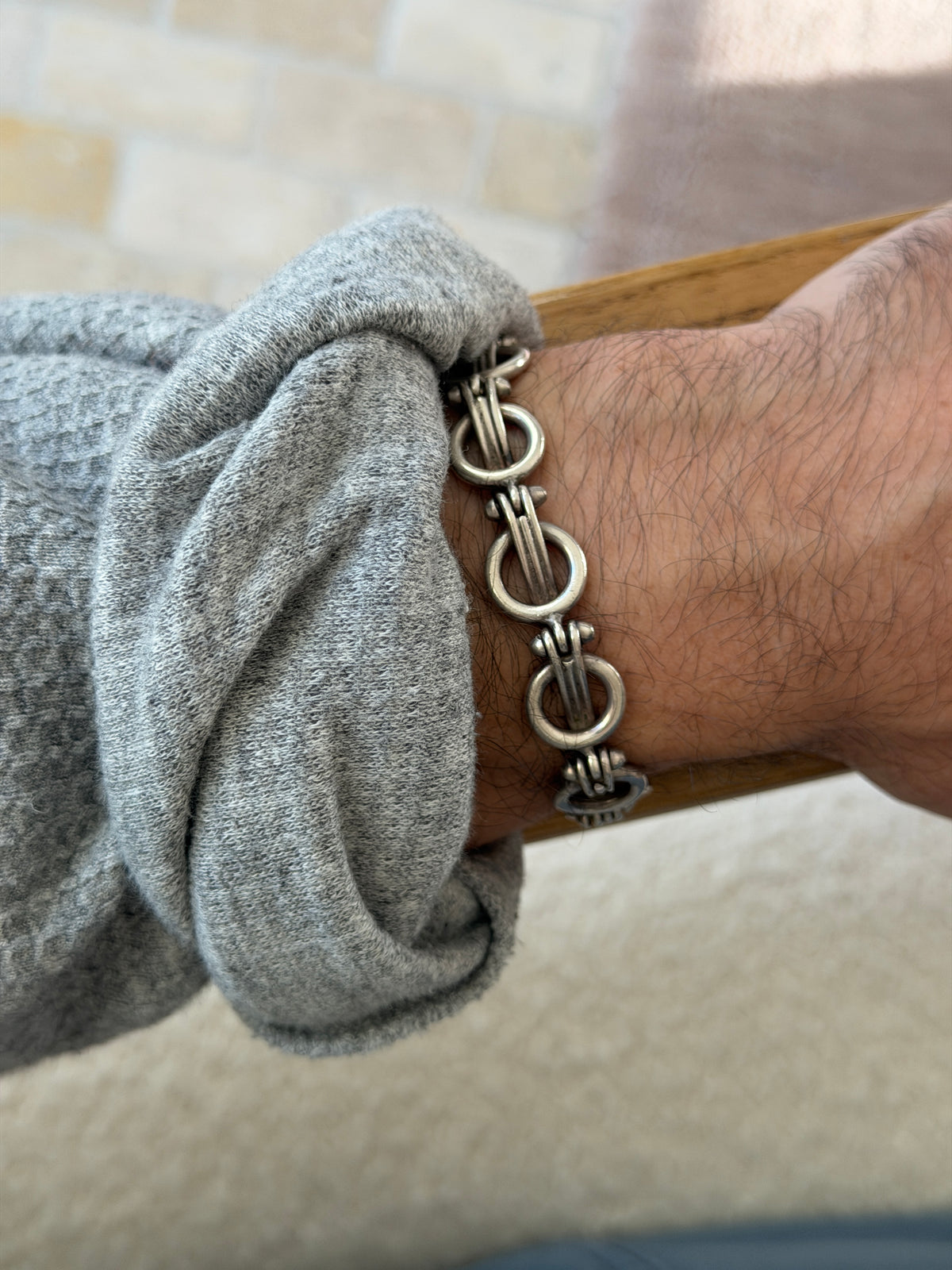 Mexican silver ring and bar bracelet on the wrist resting on a wooden chair arm, a brick wall blurred behind