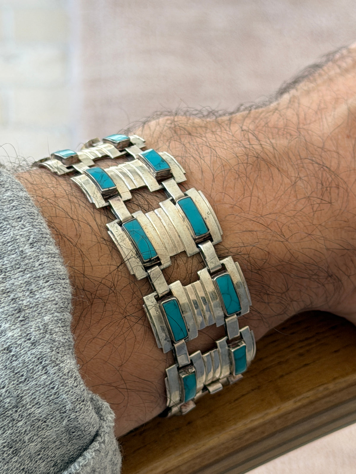 Angled view of the turquoise and silver bracelet on the wrist resting on a wooden chair arm, matrix veining visible in the stones