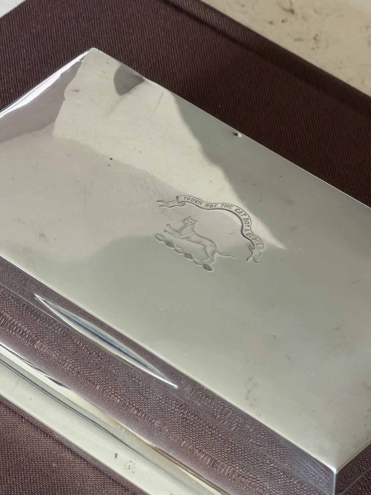 Close up of the engraved crest reading Touch Not The Cat Bot A Glove above a cat on a wreath