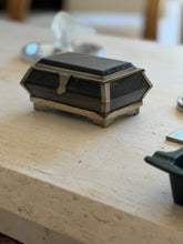 Low angle view of the casket shaped box, highlighting the angled corner mounts, shaped hasp, and stepped silver tone feet