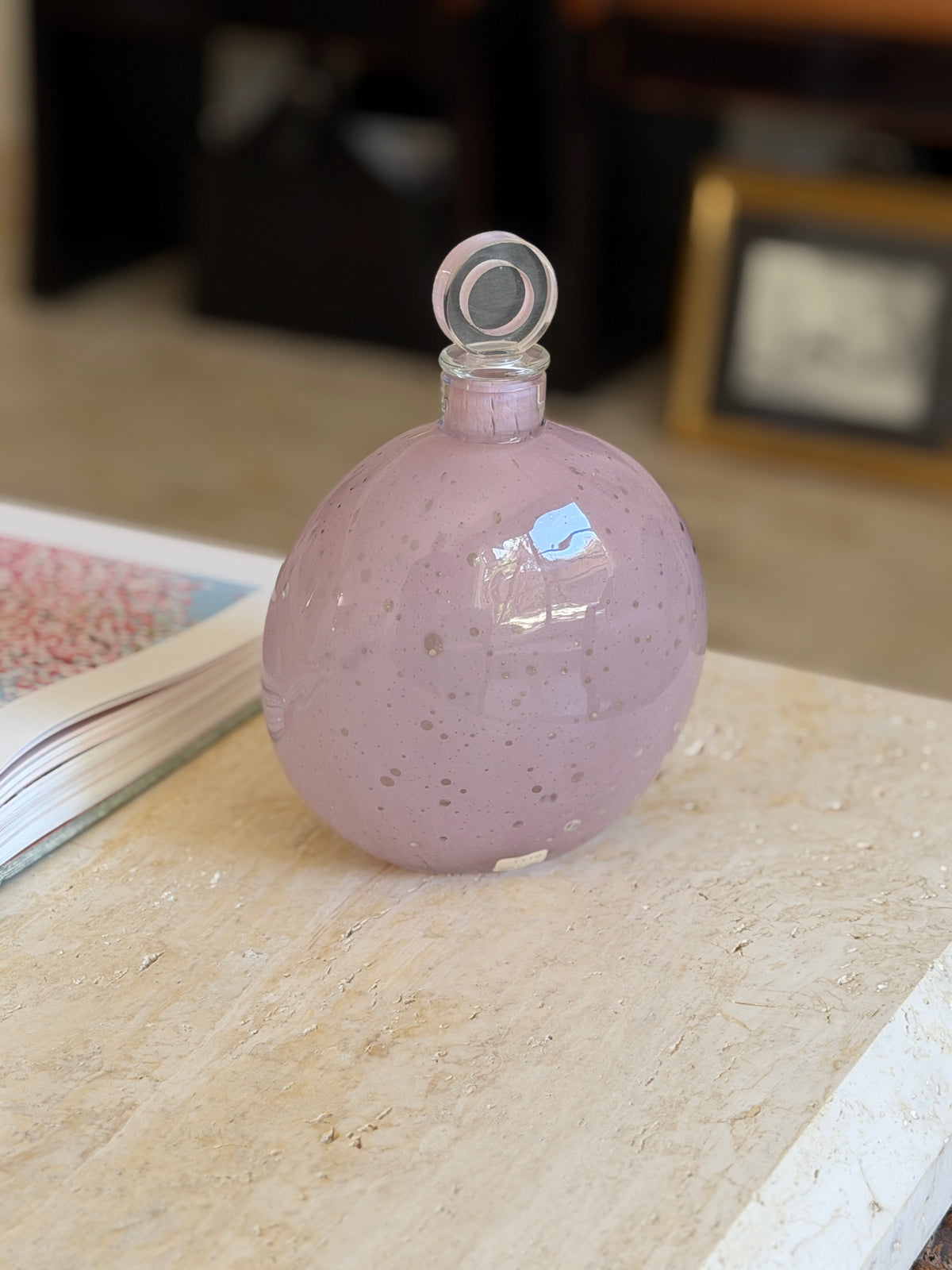 Front view of the round flat sided Murano bottle decanter, its lavender glass flecked with white inclusions and a small foil label at the base