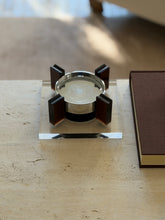 Square base magnetic floating ashtray seen at table level beside a brown clothbound book, light catching the clear Lucite edges