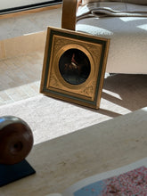 Framed jockey painting leaning against a bentwood chair on a pale carpet in afternoon sun, travertine and stone tile visible behind