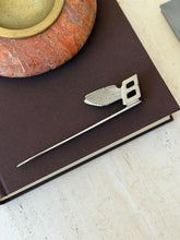Overhead view of the Bentley letter opener on a brown clothbound book beneath a red stone ashtray, the feathered wing catching the light