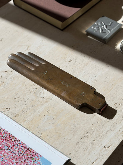French brass glove form on a travertine coffee table beside an open art book, a brown book and a pewter box with runners in relief