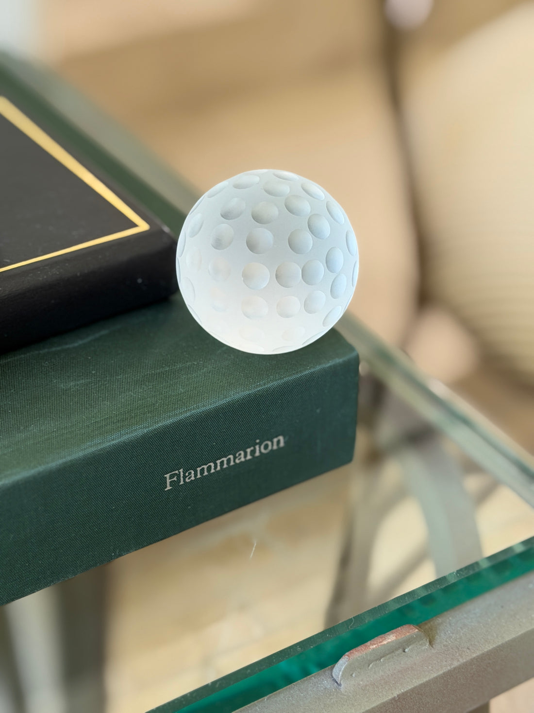 Vintage Cartier frosted crystal golf ball paperweight displayed on green display book from Collectors Gene