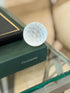 Vintage Cartier frosted crystal golf ball paperweight displayed on green display book from Collectors Gene
