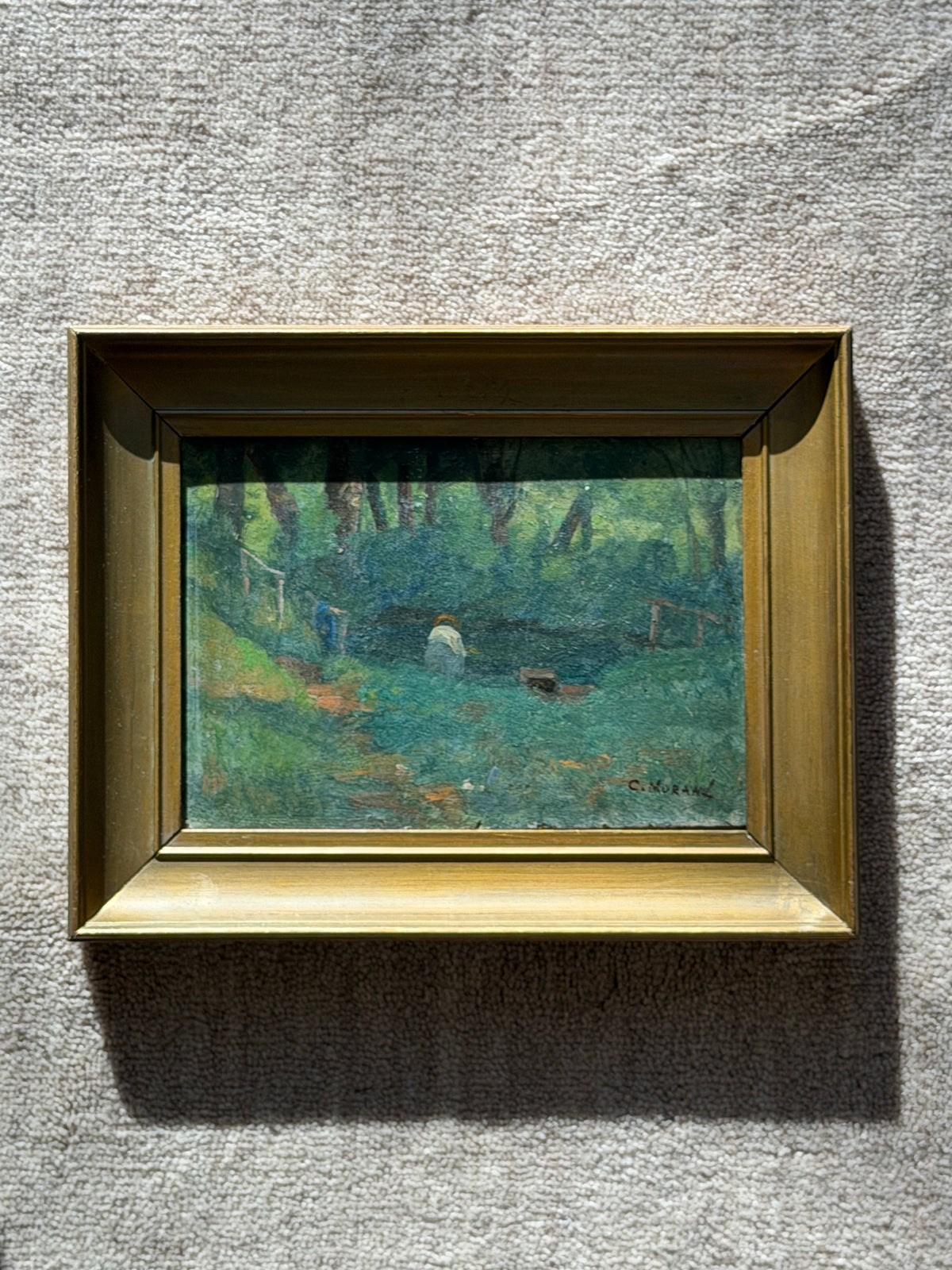 Angled close view of the woodland pond painting in sunlight, showing textured brushwork, a figure in blue by a rustic rail, and a plank footbridge at right