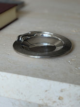Low eye level view of the Christofle dish showing the stepped ribbed band and the streamlined cigarette rest curling over the rim