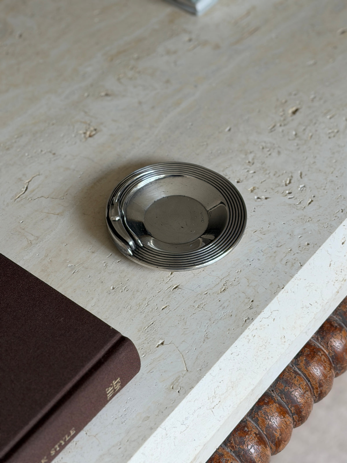 Christofle Art Deco dish near the corner of a brown clothbound book, the ribbed rim and swept rest catching soft daylight