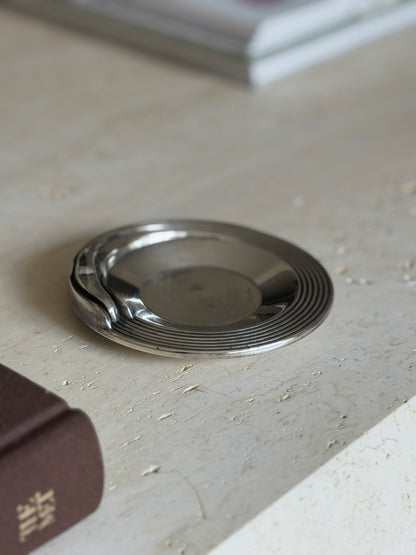 Close angled view of the Christofle dish, the automobile inspired rest and fine ribbing in focus with a book spine in the foreground