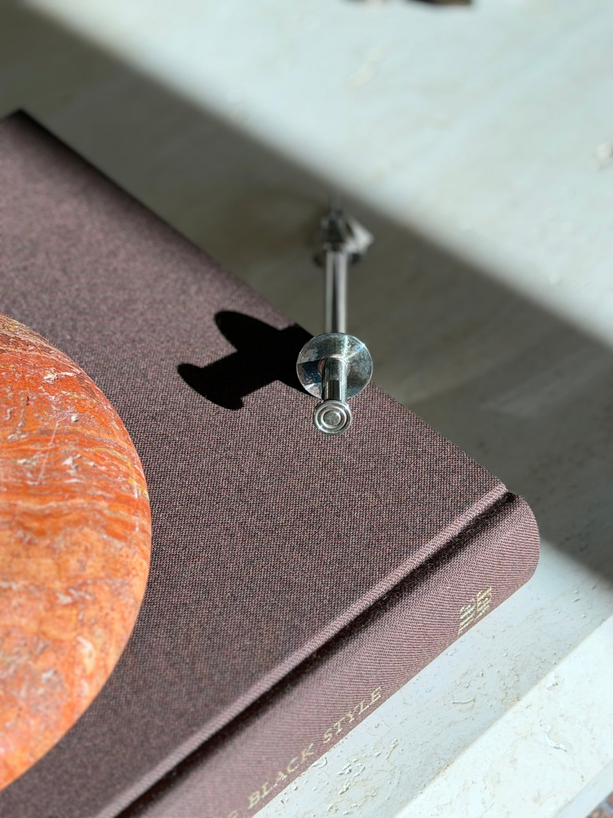 Top down view of the push button and collar disc of the Christofle mechanical tongs on a brown book beside a red stone ashtray