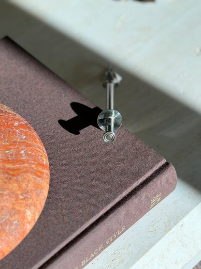 Top down view of the push button and collar disc of the Christofle mechanical tongs on a brown book beside a red stone ashtray