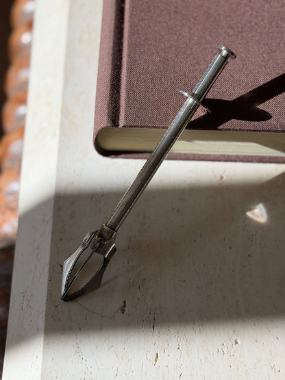 French mechanical tongs propped on a book edge, light catching the engine turned pattern and the open claw grips
