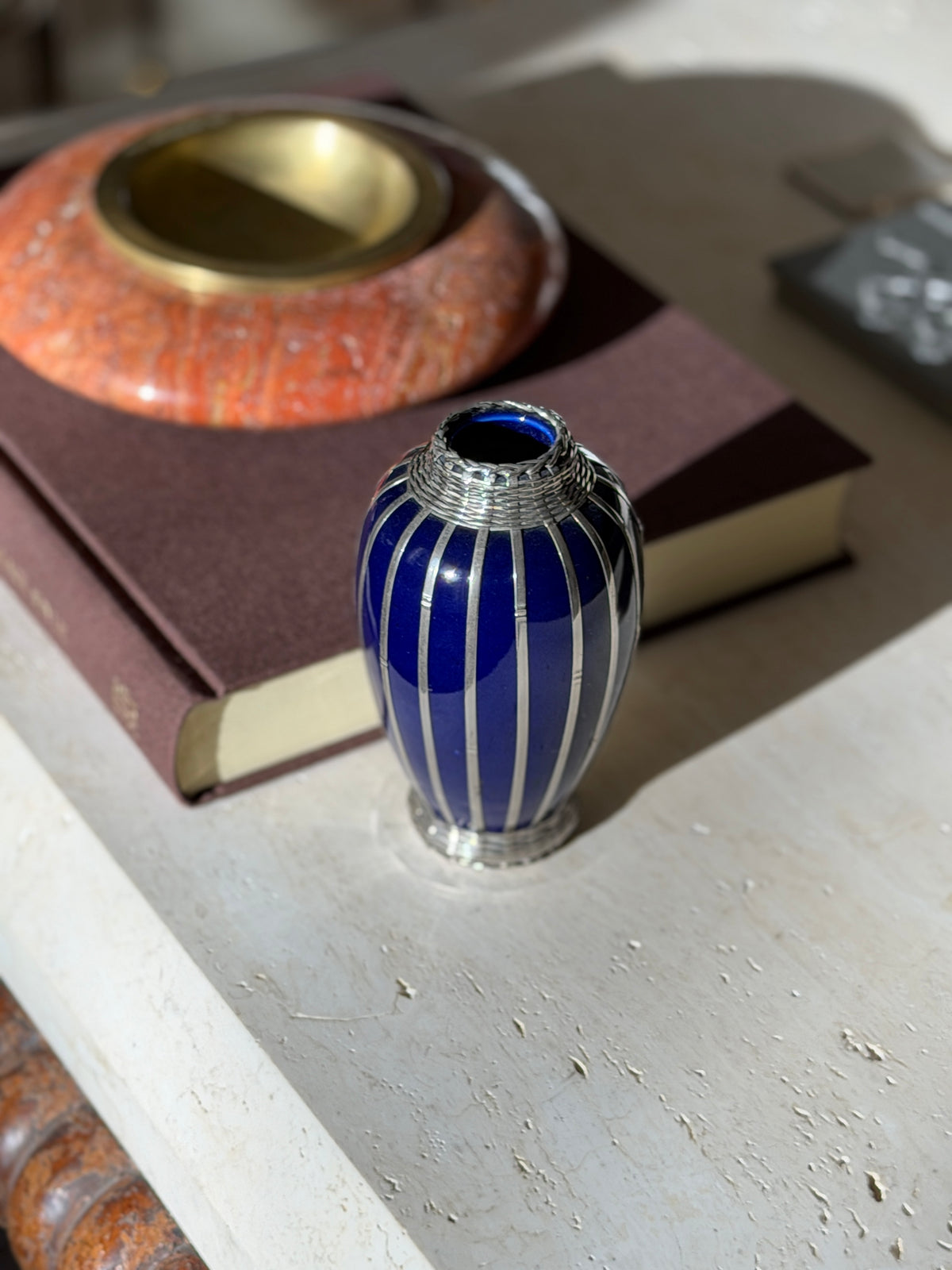 Cobalt blue Japanese vase wrapped in silver strapwork with woven silver bands at the neck and foot, beside a red stone ashtray on a brown book