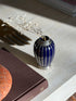 Overhead view of the silver overlay vase with dried flowers, the woven silver collar and ribbed body above a brown book