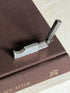 Overhead view of the open Dunhill cutter on a brown book, hallmarks visible along the top edge of the engine turned body