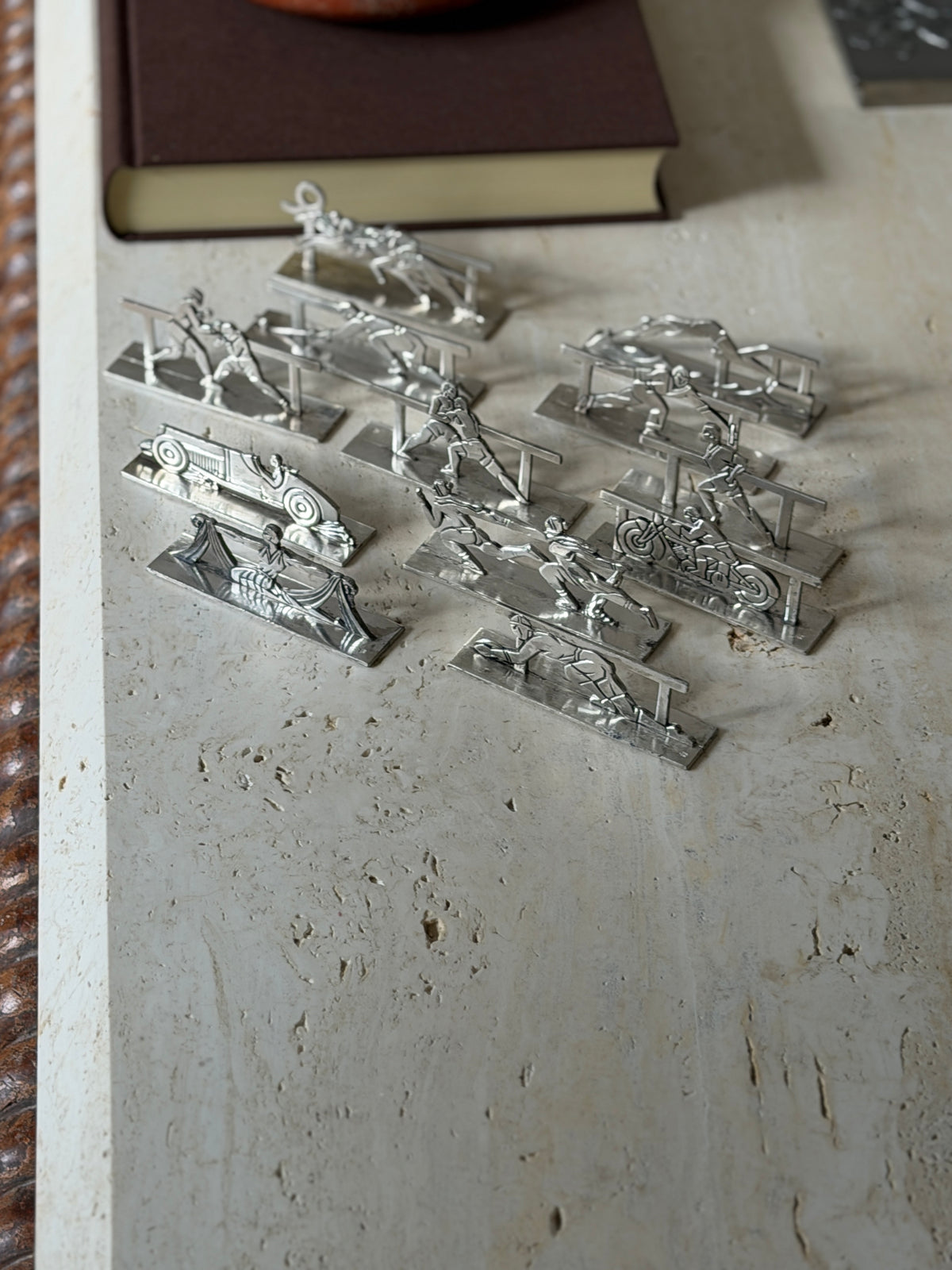Twelve French silver plate Art Deco knife rests by Pierre Devouge arranged on a travertine table, each a cutout sporting scene on a flat rectangular base