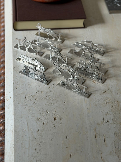 Twelve French silver plate Art Deco knife rests by Pierre Devouge arranged on a travertine table, each a cutout sporting scene on a flat rectangular base