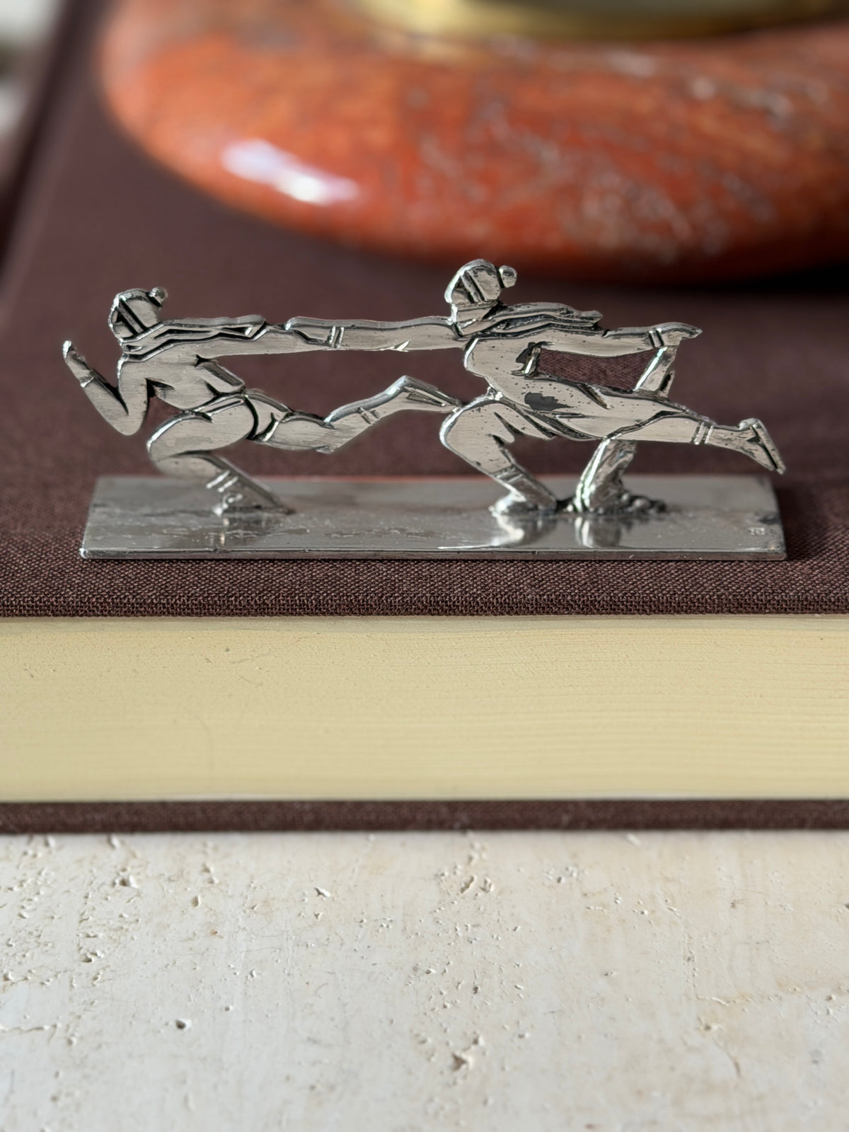Skating pair knife rest on a brown book, two figures in caps and scarves gliding hand in hand