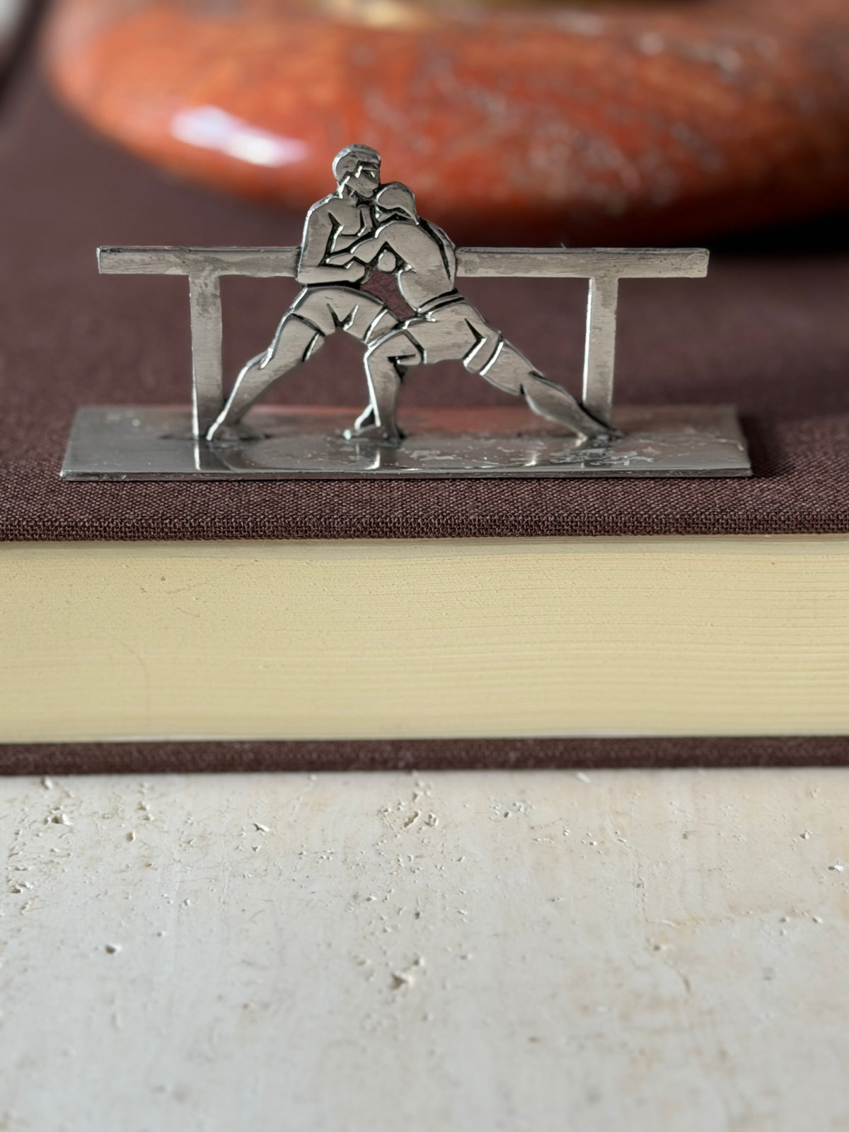 Second boxing knife rest on a brown book, two gloved fighters locked in a clinch in front of the rail