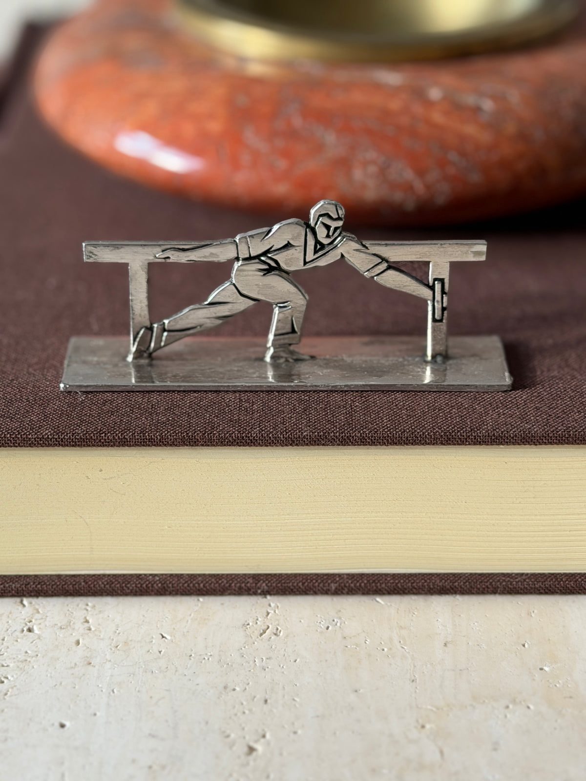 Knife rest of an athlete in a long lunge gripping the rail, set on a brown book before a red stone ashtray