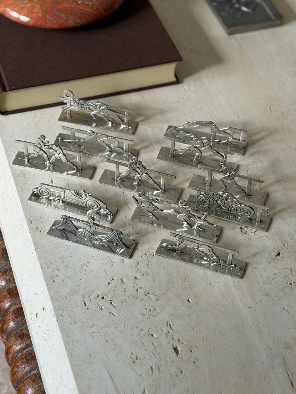 High angle view of the sporting knife rests near a brown book, showing boxers, a fencer, a race car, a motorcyclist, a jockey pair and a draped dancer