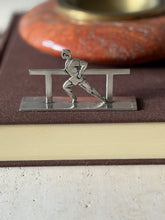 Runner knife rest on a brown book, a sprinter leaning forward mid stride against the rail