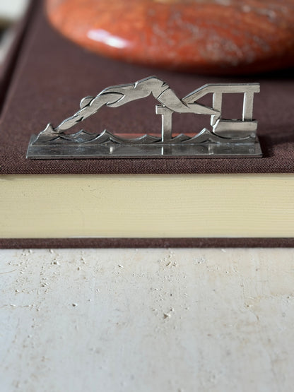 Swimmer knife rest on a brown book, a diver launching from a starting block over stylized waves