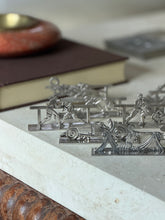 Low angle view across the knife rests, two boxers squaring off behind a rail with the race car and draped dancer in the foreground