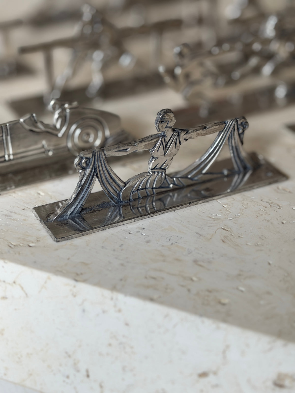 Knife rest of a kneeling dancer stretching swags of pleated drapery between her arms, in geometric Art Deco line work