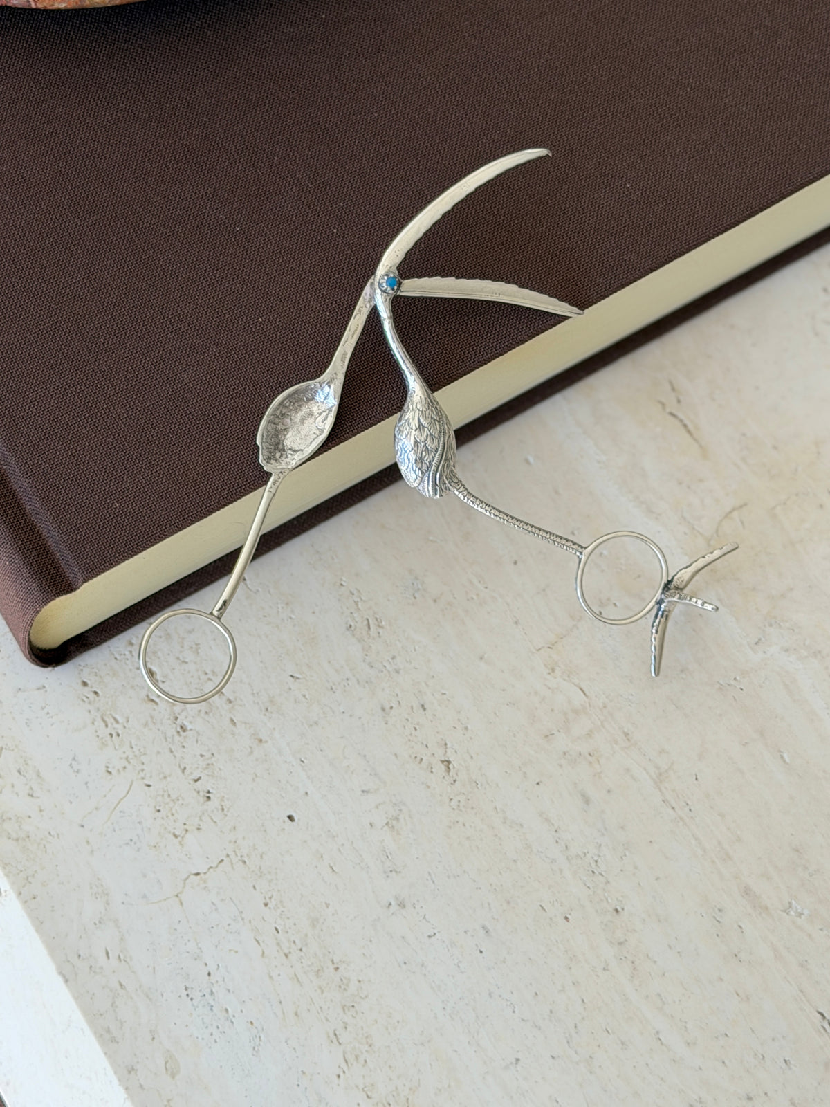 Flamingo tongs opened on a brown book, revealing the hidden spoon bowl inside the bill and the separate bird foot stand