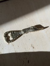 Brass duck opener in bright sunlight, the textured feathering and polished bill in sharp relief