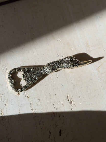 Brass duck opener in bright sunlight, the textured feathering and polished bill in sharp relief