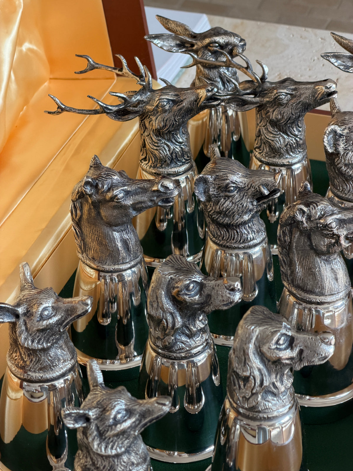Close overhead view of two stag heads with large antlers alongside boar, horse, hound, and hare cups, with Italy stamped on one cup&